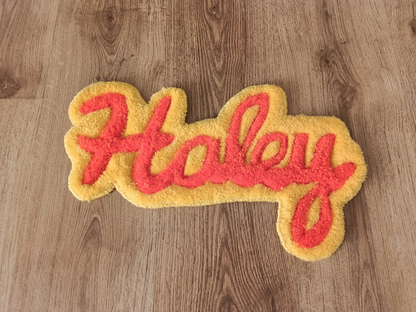 Yellow and orange tufted rug with ‘Haley’ text on a wooden floor