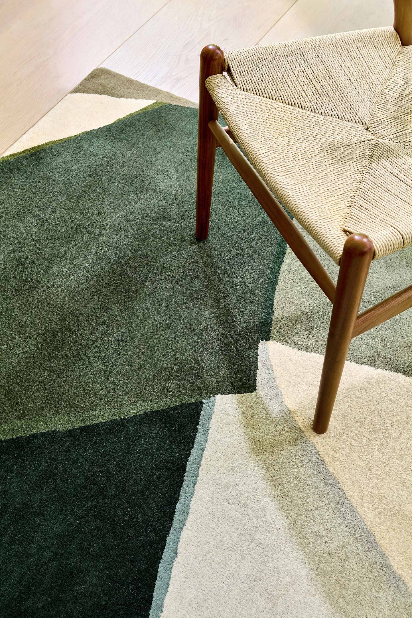 Close up corner detail of Harlequin Sumi hand tufted wool rug showing texture and geometric pattern beside chair.