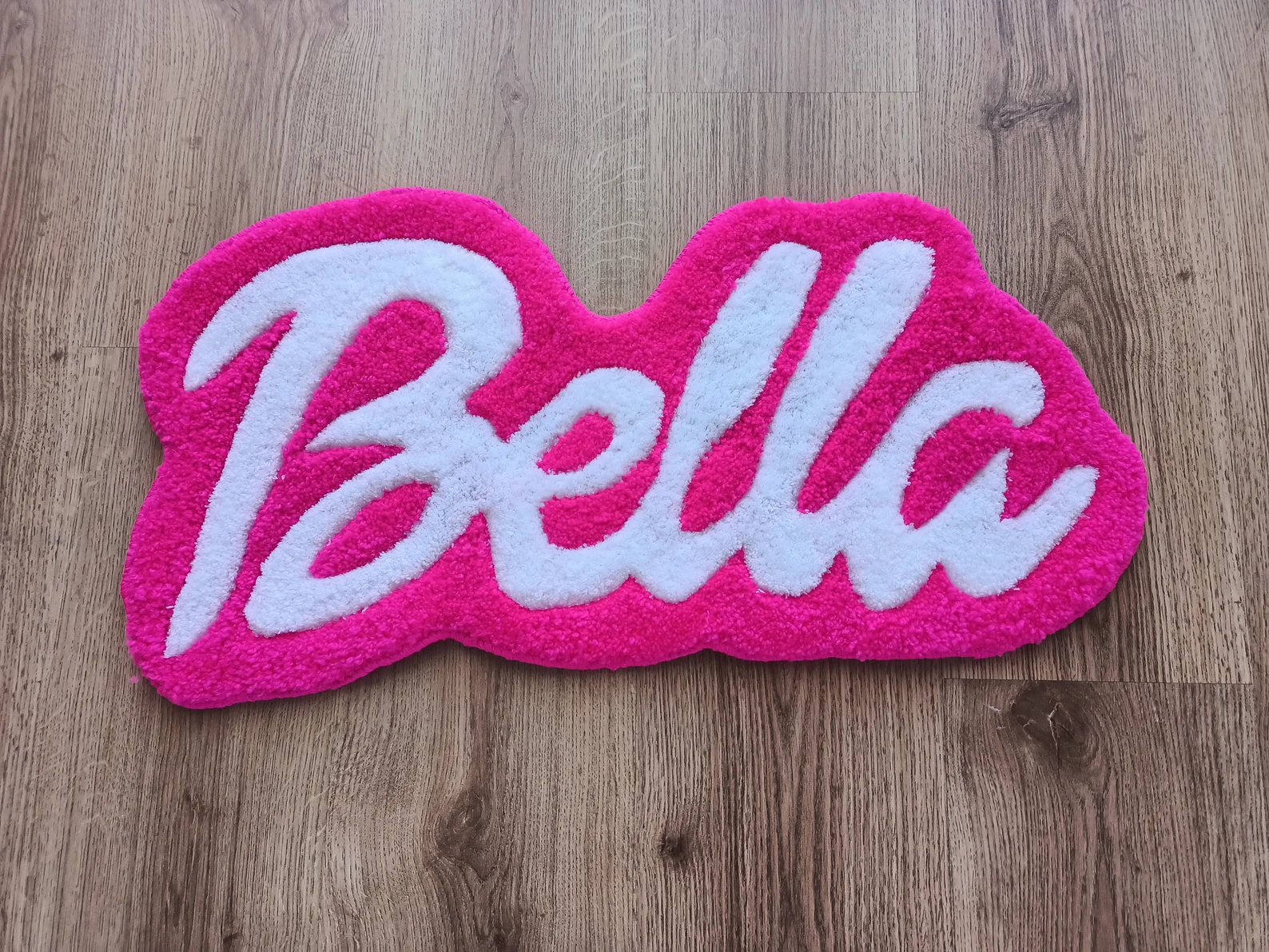 Pink hand-tufted rug with ‘Bella’ text placed on a wooden floor