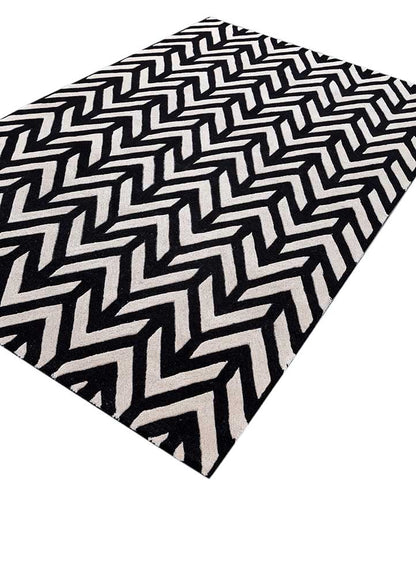 Black and ivory hand tufted wool rug showing chevron zigzag design from angled view with rich texture.