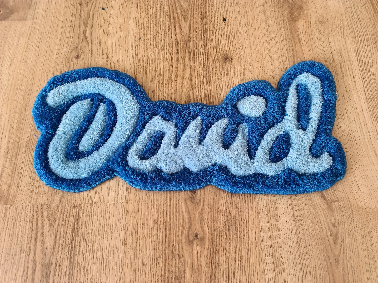 Blue hand-tufted rug featuring the name ‘David’ on a wooden floor