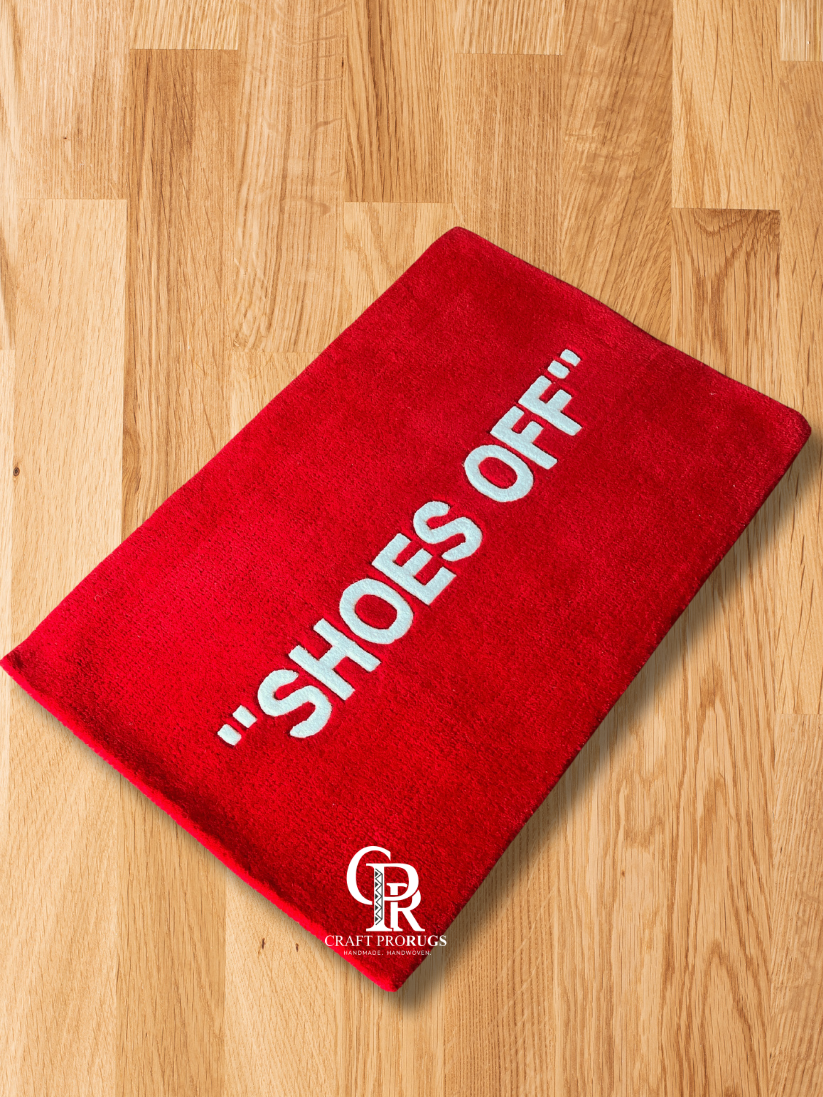 Angled view of red hand-tufted doormat with "SHOES OFF" text on wooden floor