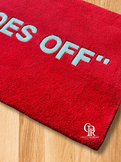 Close-up of hand-tufted red doormat showing "SHOES OFF" text and texture details