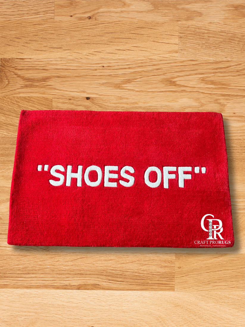 Hand-tufted red doormat with "SHOES OFF" text, placed on wooden floor in entryway