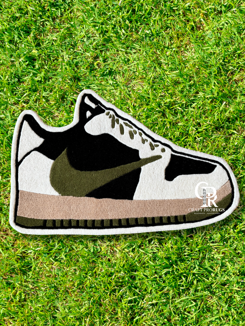 Top view of full Nike shoe shape rug in brown and olive colors placed on grass showing hand-tufted detail