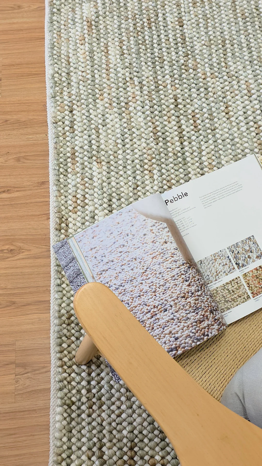Pebbles Sage Green flatweave rug in lifestyle setup with wooden furniture on hardwood floor for modern living room.